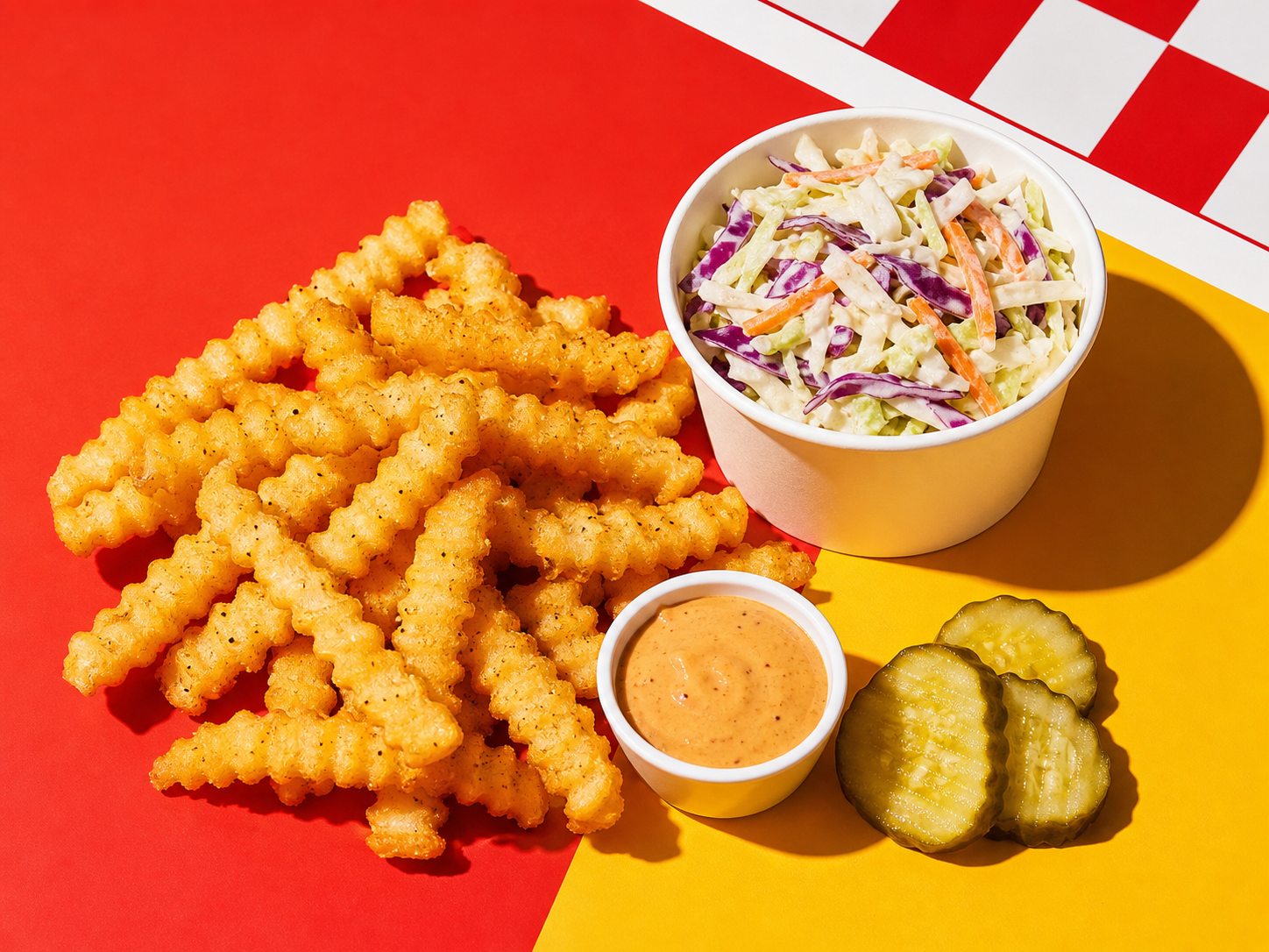 Crinkle fries, cole slaw, pickles, and sauce on a red and yellow tabletop